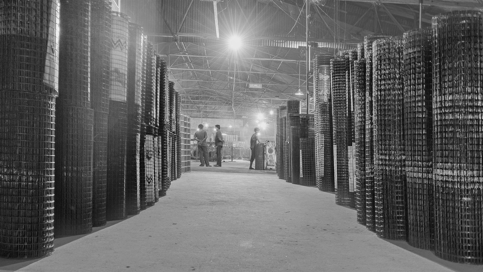 Rows of finished weldmesh rolls stacked in the MM Industries finished-stock hall in Raipur, with workers at the far end